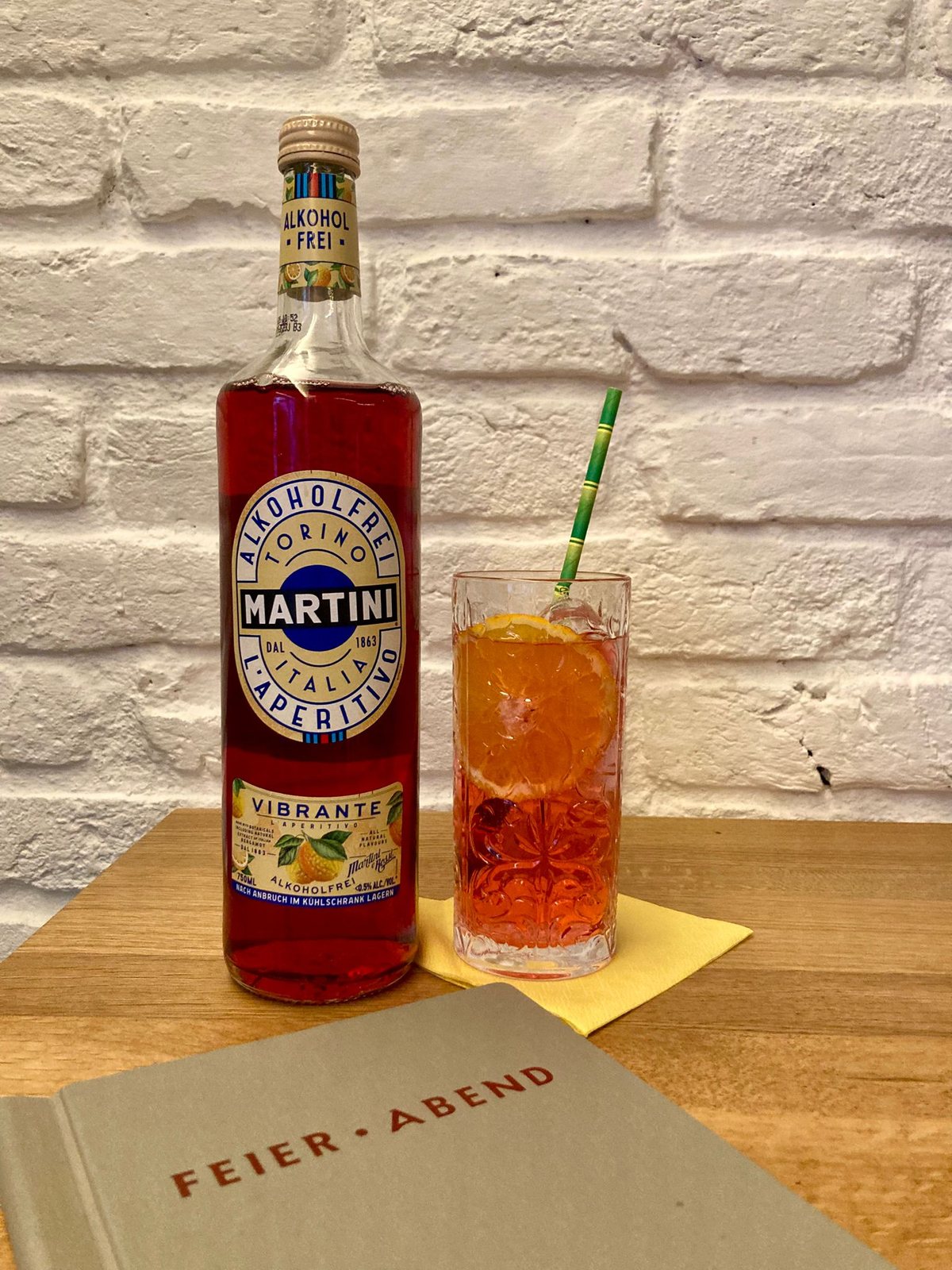 Alkoholfreier Martini Vibrante neben einem Spritz mit Orangenscheibe und Bambushalm, davor die Feier·Abend Karte