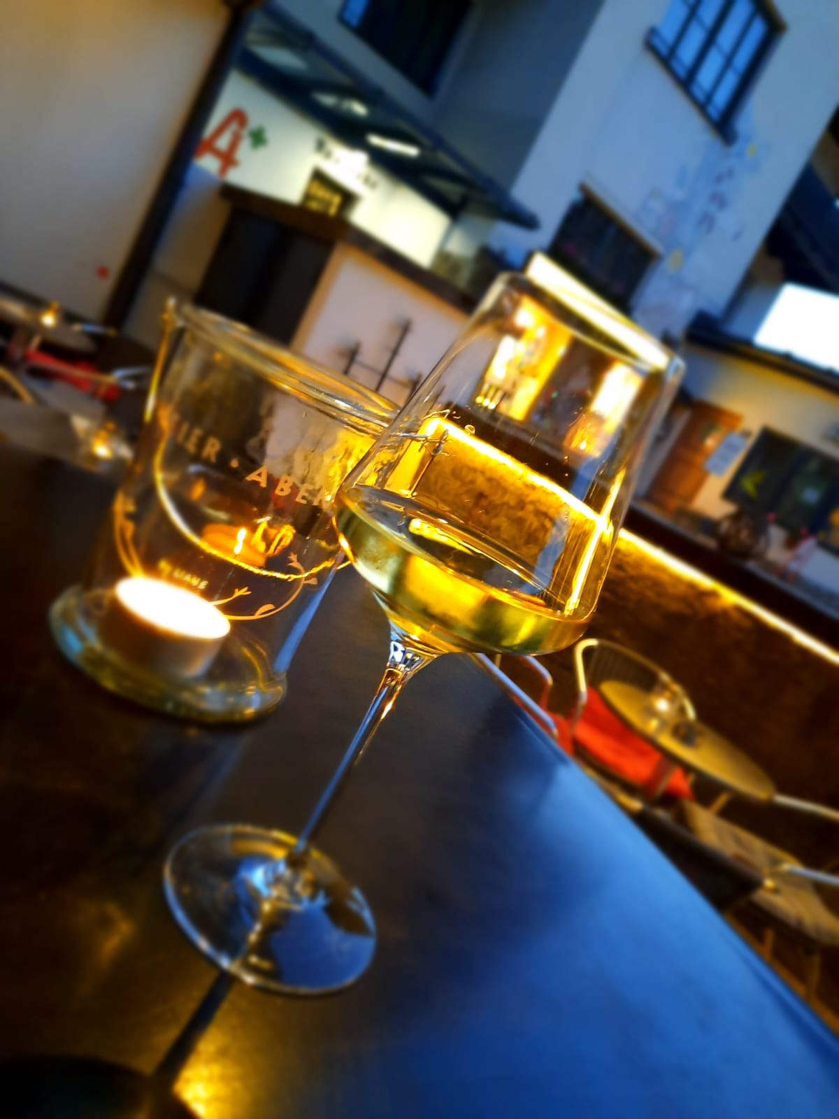 Zwei Gläser Weißwein am Tresen im Abendlicht, daneben ein Windlicht mit dem Feier·Abend Schriftzug